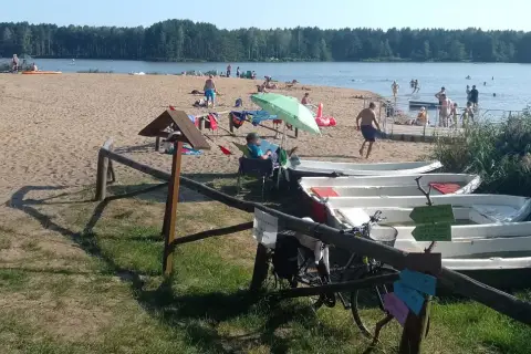 Słoneczny dzień nad zalewem zielona. Ludzie odpoczywają na plaży, kąpią się w wodzie, a obok cumują łódki.