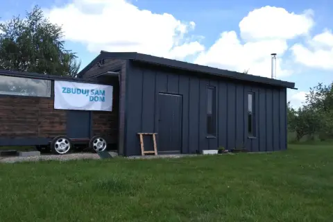 Mobilny garaż bez pozwolenia, z banerem "Zbuduj sam dom", stoi na trawie.