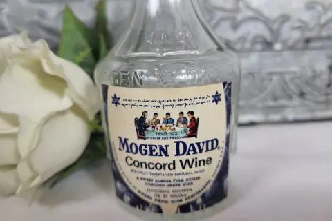 Butelka wina Mogen David Concord Wine z etykietą i białym kwiatem w tle.