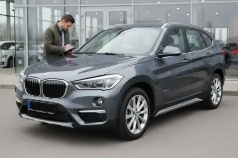 Szary BMW X1 F48 przed salonem, mężczyzna spisuje dane na kartce.
