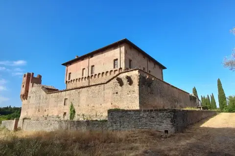 Rocche e mura antiche a Civitella Paganico cosa vedere: un castello medievale in mattoni rossi sotto un cielo azzurro, circondato da vegetazione rigogliosa.