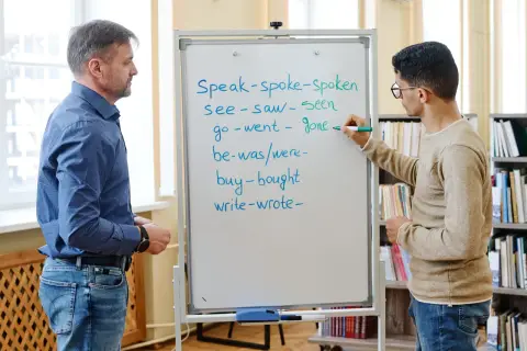 Un insegnante e uno studente studiano il passato in inglese. Lo studente scrive verbi irregolari sulla lavagna.