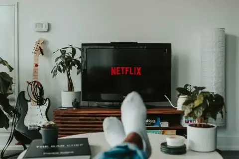 Telewizor z logo Netflix, gitara elektryczna i rośliny w salonie.