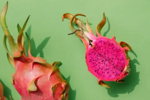 Zwei leuchtend pinke Drachenfrüchte, eine angeschnitten, zeigen ihr gesundes, kernreiches Inneres auf grünem Hintergrund.