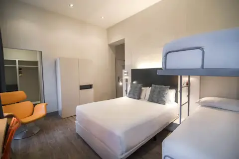 Habitación familiar en Petit Palace Canalejas Sevilla con cama doble, litera y sillón naranja.