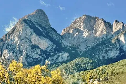 Majestuosas montañas de el Pedraforca bajo un cielo azul. El sol ilumina las cumbres rocosas y los bosques verdes.