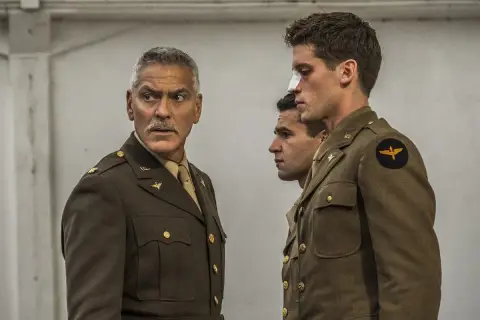 George Clooney w mundurze, obok dwóch młodych żołnierzy. Jeden z nich ma opatrunek na nosie. Scena jak z paragrafu 22.