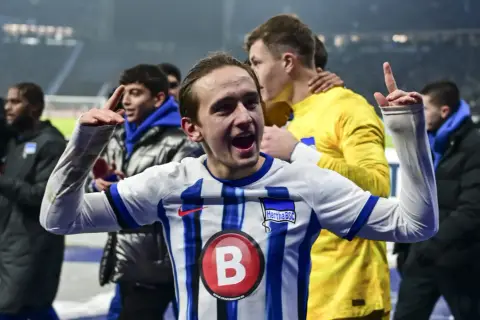 Radość zawodników Herthy BSC po zwycięstwie w 2. Bundeslidze. Młody piłkarz z uniesionymi rękami świętuje sukces.