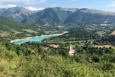 Panoramica del lago di Fiastra, con montagne verdi, un borgo e una chiesa. Cosa vedere in questo paesaggio mozzafiato.