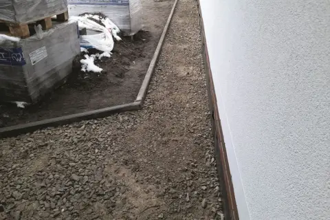 Niedokończony podjazd do domu, z paletami kostki brukowej i żwirem.