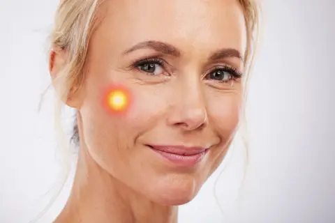 Mujer sonríe con un punto de luz roja en la mejilla, sugiriendo un tratamiento como Endolift. Consulta el endolift precio.