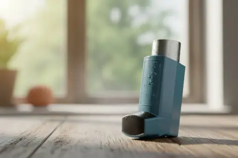 Niebieski inhalator Ventolin z kropelkami wody na drewnianym blacie, w tle okno z zielenią.