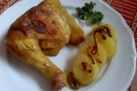Pieczone udka kurczaka z ziemniakami i natką pietruszki na białym talerzu.