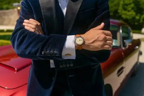 Elegancki mężczyzna w granatowym aksamitnym garniturze i białej koszuli pokazuje, jak nosić zegarek do koszuli. Klasyczny styl.