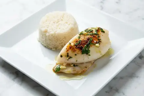Délicieuse seiche à la plancha, servie avec du riz blanc et garnie d'herbes fraîches et d'ail.