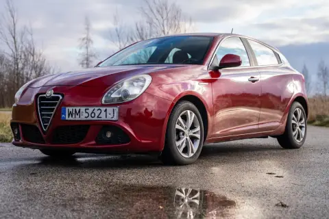 Czerwone Alfa Romeo Giulietta na mokrej drodze. Wiele osób szuka alfa romeo giulietta opinie przed zakupem.