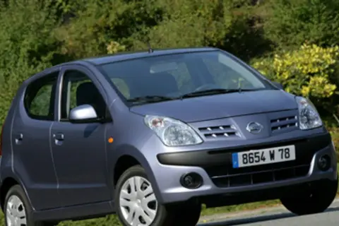 Niebieski Nissan Pixo z tablicą rejestracyjną 8654 W 78 zaparkowany na tle zieleni.