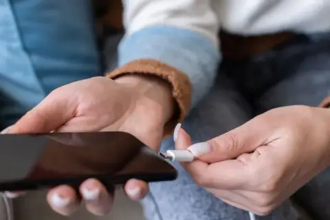 Dłoń podłącza kabel do telefonu. Zastanawiasz się, ile kosztuje wymiana baterii w telefonie?