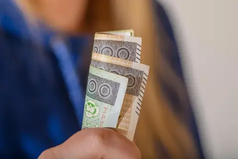 Orzeczenie o niepełnosprawności to podstawa do ubiegania się o zasiłek pielęgnacyjny. Dłonie trzymają banknoty 100 zł.