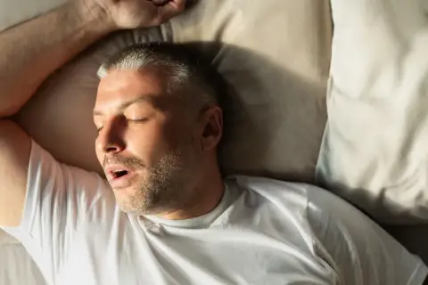 Mann schläft mit offenem Mund, was auf leichte Schlafapnoe hindeuten könnte.