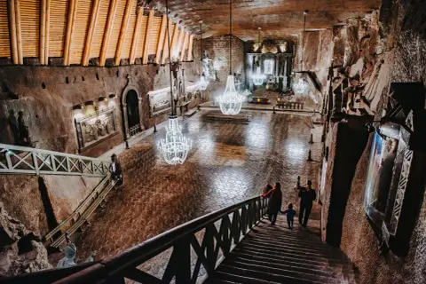 Rodzina schodzi schodami do podziemnej kaplicy w kopalni soli „wieliczka” opinie. Kryształowe żyrandole oświetlają solne rzeźby.