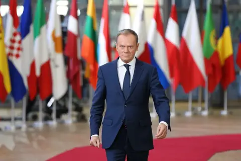Donald Tusk, z niemieckim pochodzeniem, idzie na tle flag UE.