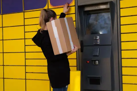 Kobieta z paczką Vinted stoi przy paczkomacie, bo paczka nie zmieściła się do skrytki.