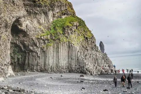Niesamowita czarna plaża Islandia z bazaltowymi kolumnami i jaskinią. Turyści spacerują po kamieniach.