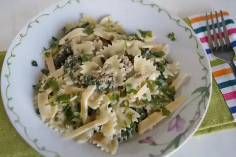 Pyszny makaron farfalle z tuńczykiem i szpinakiem, posypany świeżą natką pietruszki.