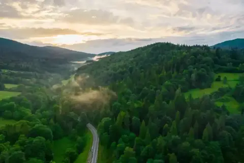 Mgła snuje się nad zielonymi dolinami, a kręta droga wije się przez gęste lasy. Bieszczady góry budzą się do życia o wschodzie słońca.