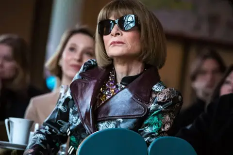 Anna Wintour w okularach przeciwsłonecznych i wzorzystej kurtce, ikona Vogue, wpatruje się w dal.