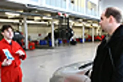 Mechanik w czerwonym kombinezonie omawia z klientem kwestie związane z ekologicznym paliwem, takim jak biodiesel, w warsztacie samochodowym.