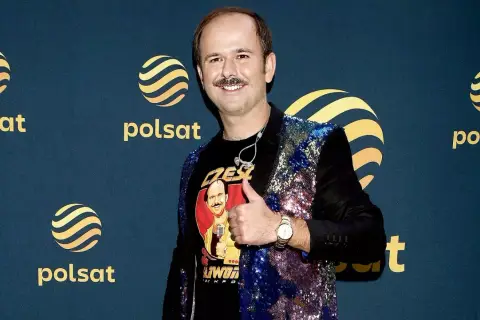 Sławomir Zapała w błyszczącej marynarce i koszulce z własnym wizerunkiem, pokazuje kciuk w górę.