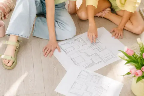 Dwie osoby analizują plany domu, przygotowując się do uzyskania pozwolenia na budowę.