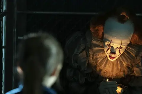 Przerażający klaun Pennywise z "To" w jednym z najlepszych horrorów ostatnich lat, świeci sobie zapalniczką.