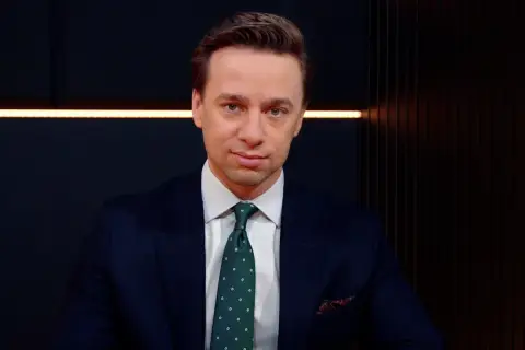Krzysztof Bosak w garniturze, z zielonym krawatem w kropki. Mówi o tym, dlaczego uważa, że polska polityka zagraniczna nie jest asertywna.