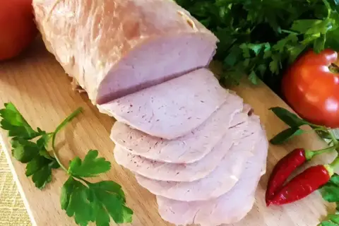 Pokrojony schab gotowany 2 razy po 10 minut, podany z pomidorami, papryczkami chili i natką pietruszki na desce.