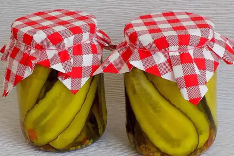 Słoiki z ogórkami w curry ze skórką, ozdobione czerwono-białymi kratkowanymi chusteczkami.