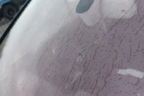 Pęknięta szyba w aucie z widocznym punktowym uszkodzeniem i pajęczyną pęknięć. Krople deszczu spływają po powierzchni.