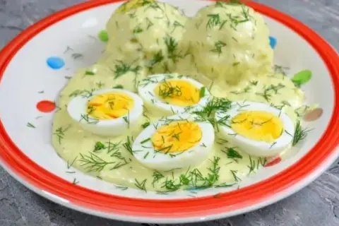 Pyszne jajka w sosie chrzanowym, udekorowane świeżym koperkiem, podane na talerzu z kolorowymi kropkami.
