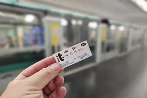 Dłoń trzyma bilet na metro paryskie. W tle widać pociąg metra.