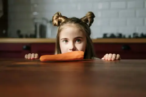 Bambina con acconciatura a ciambella guarda una carota, forse un caso di neofobia alimentare.