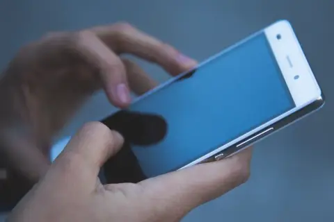 Dłonie trzymają telefon zmarłej osoby, przeglądając ostatnie wiadomości.