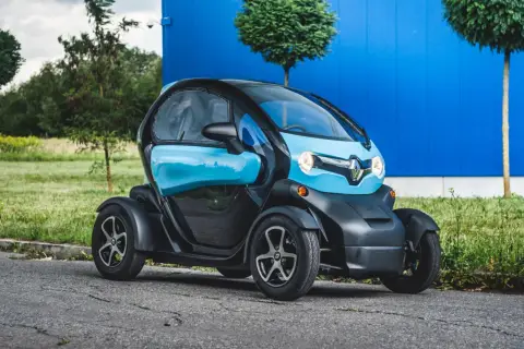 Niebiesko-czarny Renault Twizy stoi na drodze przed niebieskim budynkiem.