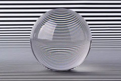 A glass sphere distorts black and white stripes, creating a mesmerizing optical illusion art piece.