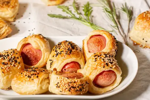 Délicieux feuilleté saucisse, dorés et parsemés de graines de sésame, sur une assiette blanche.