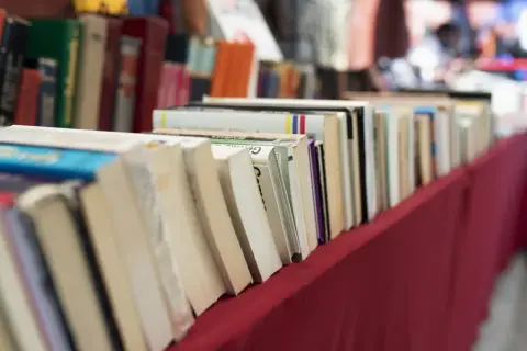 Rząd książek na czerwonym obrusie. Jak przygotować się do targów książki jako autor i czytelnik?