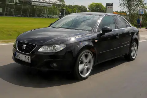 Czarny Seat Exeo 2.0 TDI w ruchu, z widocznym salonem Audi w tle.