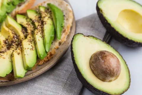 Avocado-Toast mit Gewürzen und frischem Basilikum. Ist Avocado Obst oder Gemüse? Botanisch ist sie eine Frucht, kulinarisch oft als Gemüse verwendet.
