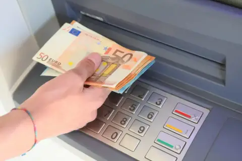 Dłoń trzyma banknoty 50 euro, walutę Hiszpanii, przy bankomacie.